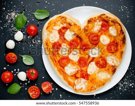 Pizza Margherita shaped heart with cherry tomatoes, mozzarella and basil - concept of romantic love for Valentines Day top view