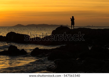 Silhouette of girl take a photo sunset on the rock and the beach