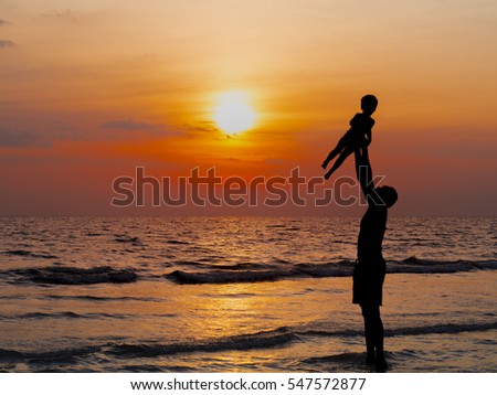 silhouettes of father and son play at sunset beach. Happy family concept