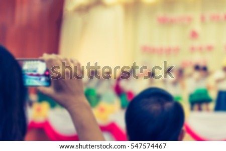 blur image of parent take photo of kid 's show on stage with smartphone at school for background usage .