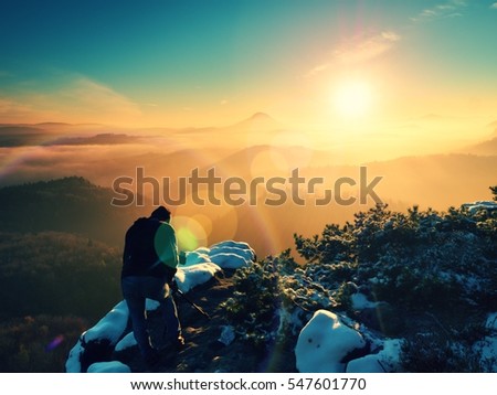 Professional photographer takes picture of freeze autumnal daybreak, rocks covered with fresh powder snow. Stony rock peak increased from foggy valley.  Lens flare effect.