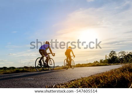 Two men ride on bike on the road. Sport and active life concept sunset time. Couple of men riding on  bicycle in a park. Blue sky with orange sun beam over the body of cyclist.