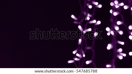 Soft abstract bokeh background. Dark copy space in left half to add text. Blurry Luminous garlands of electric lights. The gentle tone purple. Dark night. Festive party. Christmas. New Year.