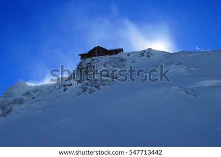 Building house for skiers skiing on the top of a snowy mountain with blue sky in background