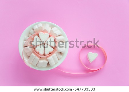 Marshmallows in heart shapes for Valentines day in white ceramic bowl over pink paper background with cute ribbon to show sweet love candy for couples on special time in holiday season