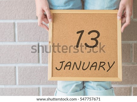 Closeup calendar at the cork board in hand of asian woman in front of her legs with 13 january word on brick wall textured background