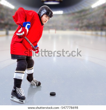 Junior ice hockey player handling puck on ice with arena full of fans in the stands and copy space. Focus on player and deliberate shallow depth of field on background.