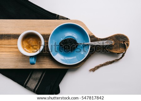 Delicious fresh morning coffee with beautiful thick crema, glasses and a spoon full of Ossetra black caviar, on the rustic wooden board background, horizontal photo