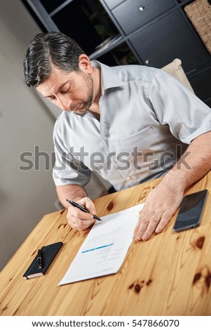 Writing business man at table signing document shot at a side perspective