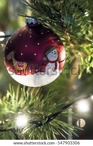 Christmas ball with the picture of deer and snowman on a pine tree with Christmas lights.