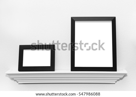 Two blank black picture frames on a picture display ledge attached to a wall