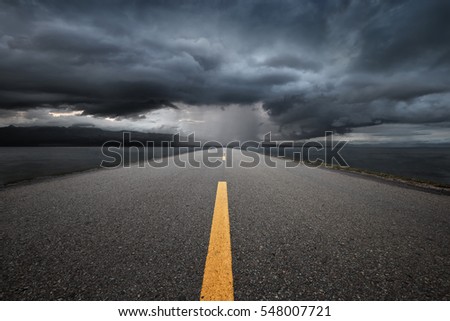 Empty highway leading to the mountains through the rain on a background of dark storm clouds
