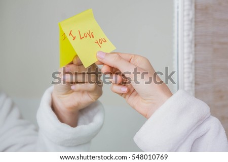 Woman sticking I love you word sticky note on mirror