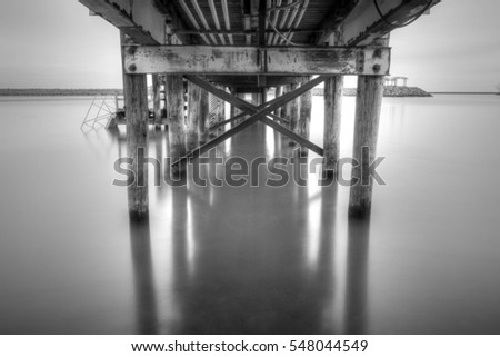 Long exposure black and white daytime picture of wooden dock with metal bracing extending out into Lake Erie with stone seawall in background in Buffalo, New York