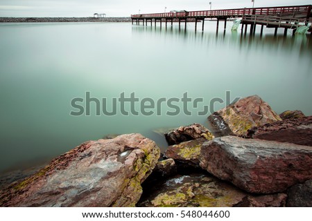 Daytime long exposure winter picture of stones in foreground and green water of Lake Erie and dock in background in Buffalo, New York