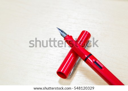 a modern red fountain pen with blue ink on wood desk