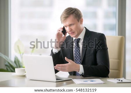 Young handsome businessman working with laptop at desk in the modern office, talking on phone, unexpected obstacles, risky business, getting a second opinion from another entrepreneur in whom confide Royalty-Free Stock Photo #548132119