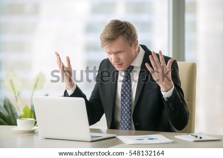 Young stressed handsome businessman working at desk in modern office shouting at laptop screen and being angry about financial situation, jealous of rival capabilities, unable to meet client needs Royalty-Free Stock Photo #548132164