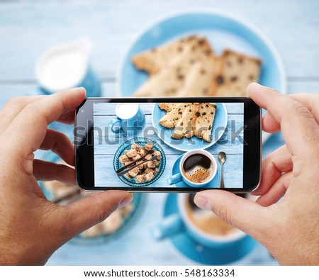 Taking photo of one's breakfast with cup of coffe by smartphone.  Closeup view of  process. File contains clipping paths for smartphone and hands and  picture on it.