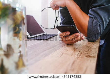 businessman hand with eyeglasses using smart phone,mobile payments online shopping,omni channel,digital tablet docking keyboard computer,flower glass vase on wooden desk,filter