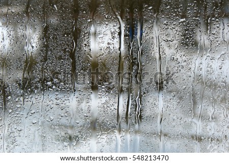 Raindrops on the glass and blurred park in the snow