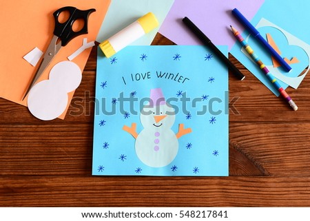 Child made a funny paper snowman applique, drew a snowflake and wrote I love winter. Stationery, colored paper sheets on a table. Paper snowman arts and crafts project diy for winter season. Top view
