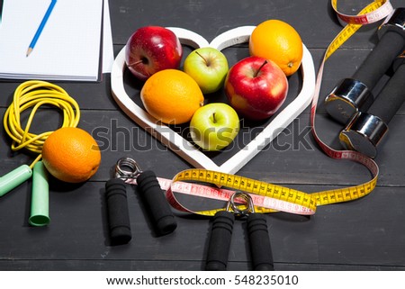 Heart, fruit and dumbbells. Fitness, healthy lifestyle on a black wooden background