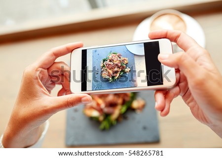 food, culinary, technology and people concept - woman hands with smartphone photographing prosciutto ham salad on stone plate at restaurant