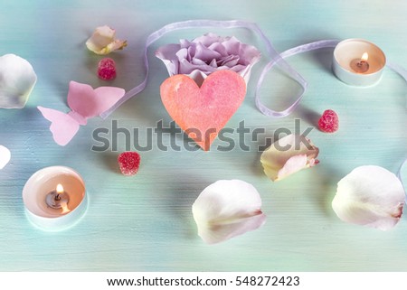A Valentine day card with a rose flower, a paper butterfly, sweets, candles, and a little cutout heart, slightly toned
