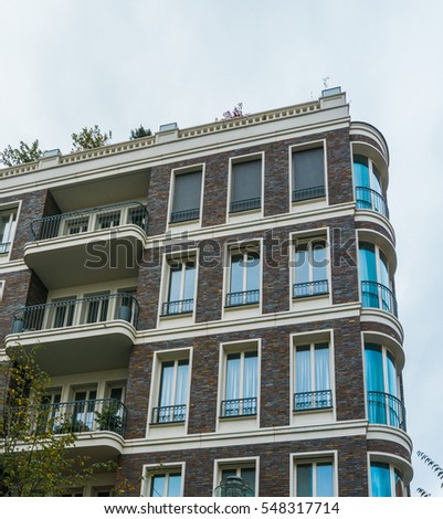 Low Angle Architectural Exterior of Urban Residential Apartment Building with Rounded Corner, Balconies and Rooftop Garden on Overcast Day