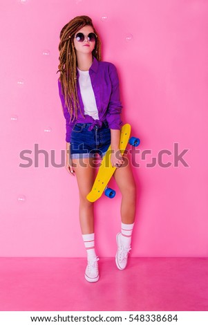 Pretty girl with dreadlocks and sunglasses holding yellow skateboard and smiling