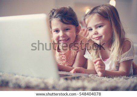 Two little sisters lying on the floor at living room and using laptop.