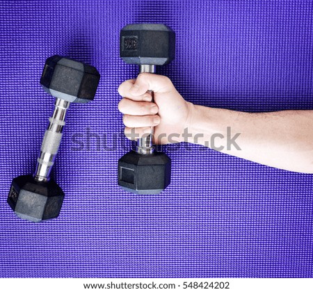 Two dumbbells with one Asian man's hand lifting one, on purple blue yoga mat background.Workout equipment.