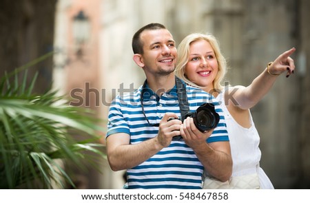 young smiling couple looking curious and taking pictures outdoors in trip. Focus on man
