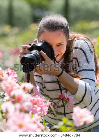 female photographer taking photo of  flowering roses in summer day