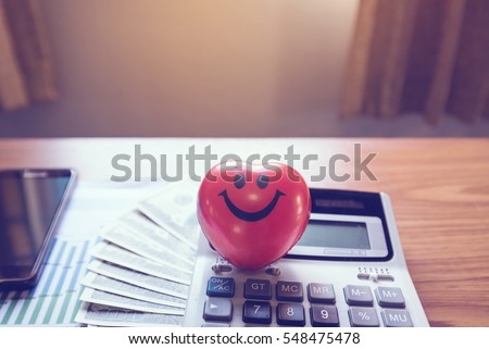Heart-shaped smiley with money, calculator, mobile phone on the desk in the office.