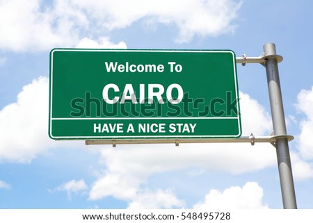 Green overhead road sign with a Welcome to Cairo, Have a Nice Stay concept against a partly cloudy sky background.