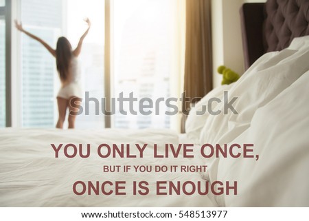 Close up of a made bed, bedding, staples quilts pillows, woman stretching near the window. Photo with motivational text "You only live once, but if you do it right once is enough"