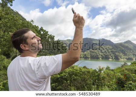 Man searching for mobile connection. No connection in wild nature. Forest and lake landscape in sunny day. Man making mobile photo. Using smartphone on vacation. No communication on holiday concept 