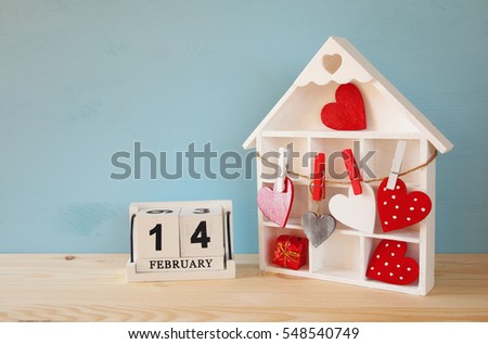 Valentines day background. Doll house with many hearts next to wooden calendar on the table