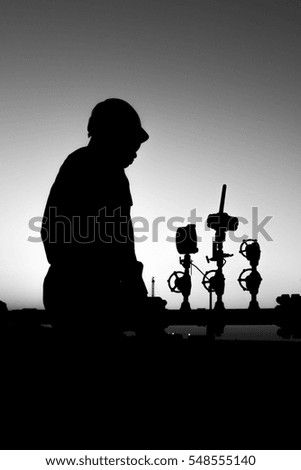 Silhouette of oilfield worker monitoring valves at sunset.
