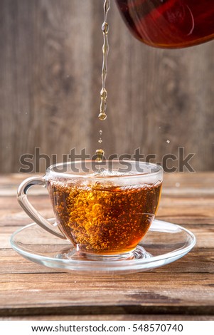 Tea in transparent cup with saucer standing on wooden table