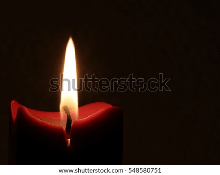Burning Candle Against Dark Background with Tall Flame - Photograph of a red colored candle burning against a dark background with a tall straight flame. 