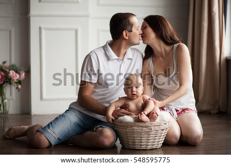 Happy young parents close to small baby in wicker basket. Parents kissing and hugging their child. 