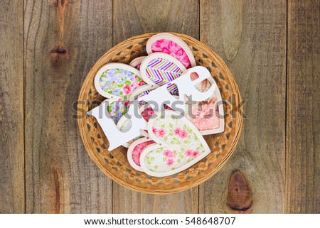 Colorful country fabric hearts and the word Love in natural wicker basket with antique rustic wood background; Valentine's Day, Mother's Day and love concept with wooden copy space