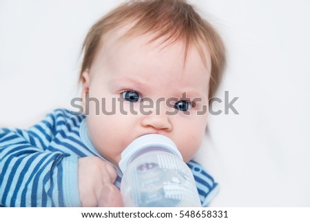 The baby is the third month from birth drink water from a bottle. Dad gives baby a bottle.