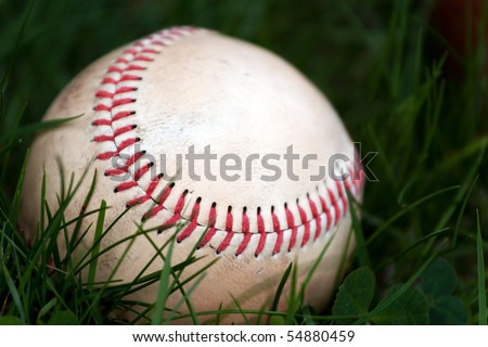 One aged and worn baseball sitting in the green grass.