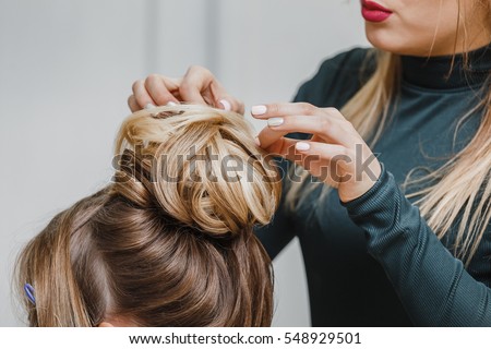 Hairdresser makes upper bun hairstyle close-up on brown hair of beautiful woman Royalty-Free Stock Photo #548929501