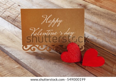 Valentines day background. Couple of red hearts next to letter with text: HAPPY VALENTINES DAY on wooden table. Filtered image