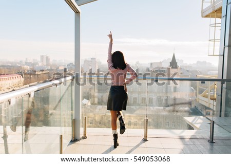Stylish modern city image of attractive young woman from back having fun on terrace in sunny morning. Big city life, great success, business, happiness, good luck, positivity
